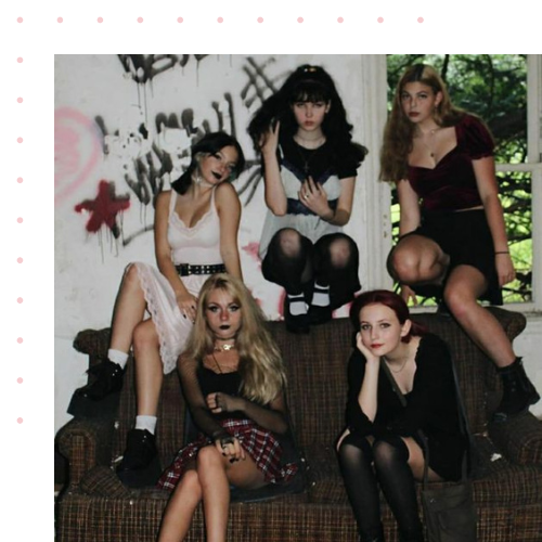 A group of girls that are all dressed in alternative black clothes sitting on a couch