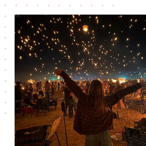 A girl standing in a field with floating lanterns that are in the night sky