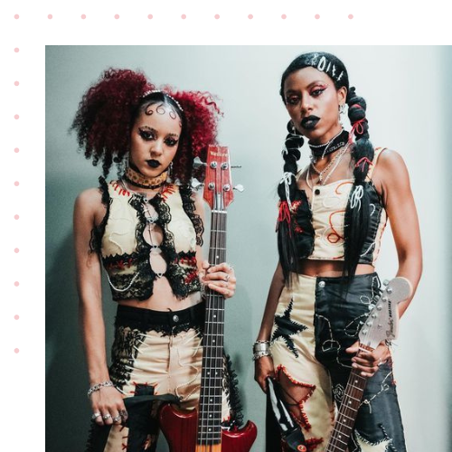 Two women holding guitars wearing handmade looking clothes